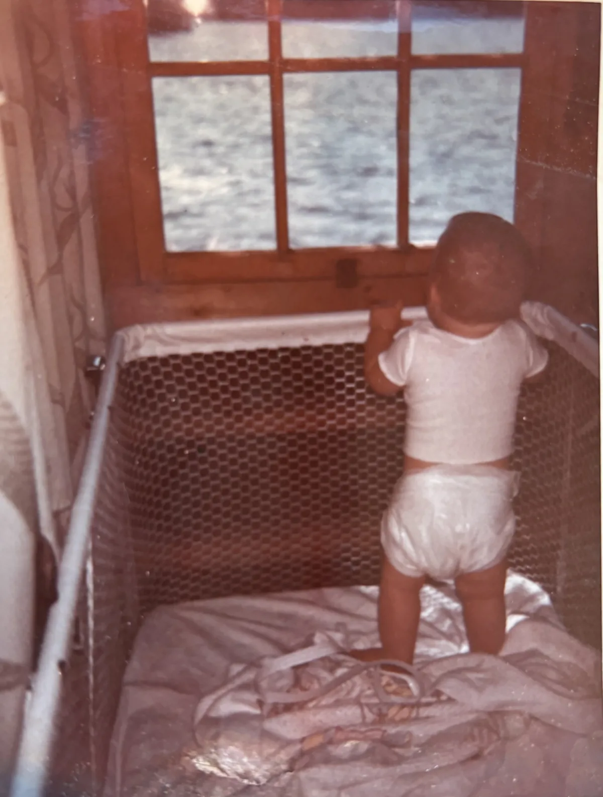 Robert at nine months, standing in a playpen and looking out a window at Northern Light Lake